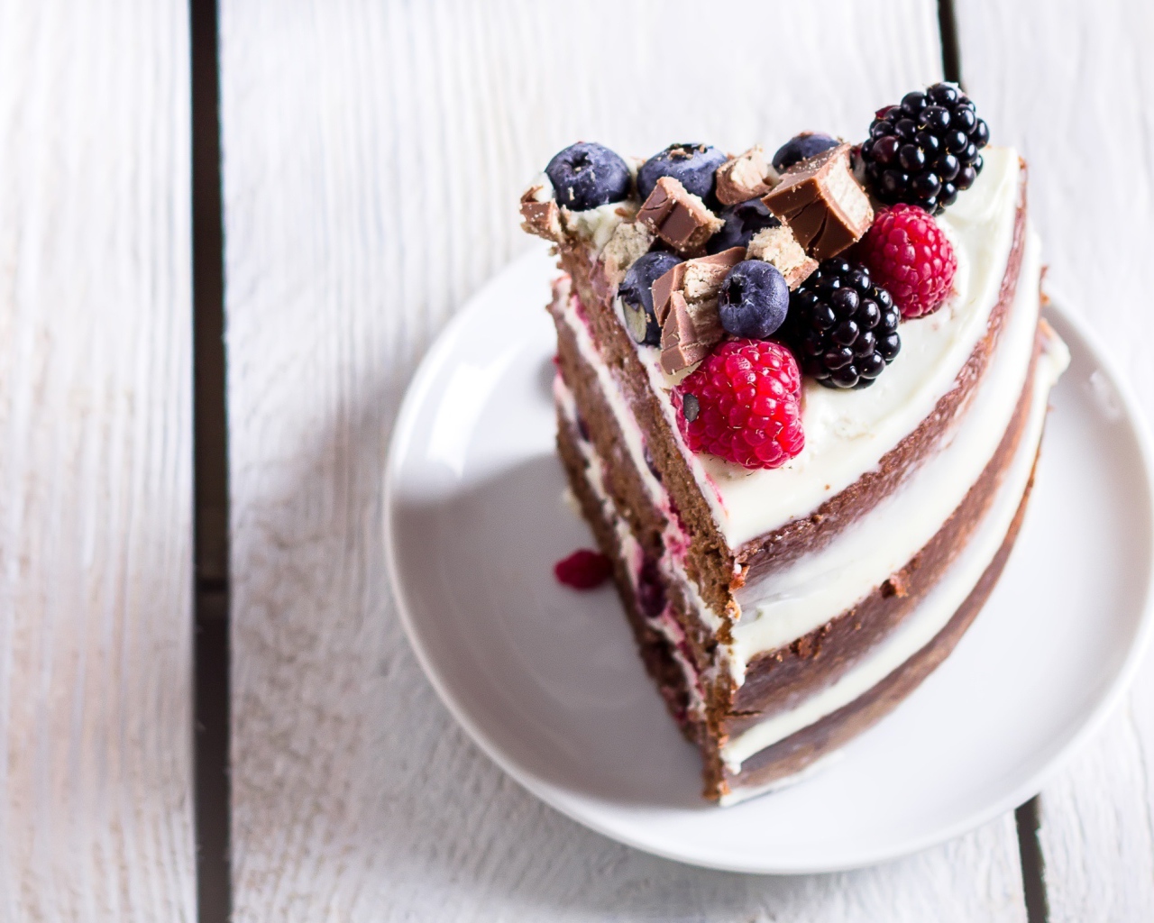 Кусок торта с ягодами малины и черники на блюдце