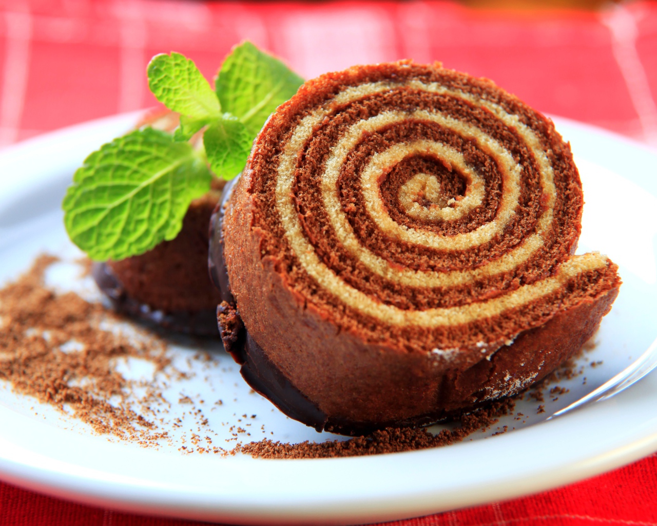 Кусок сладкого рулета с шоколадом и листом мяты на тарелке