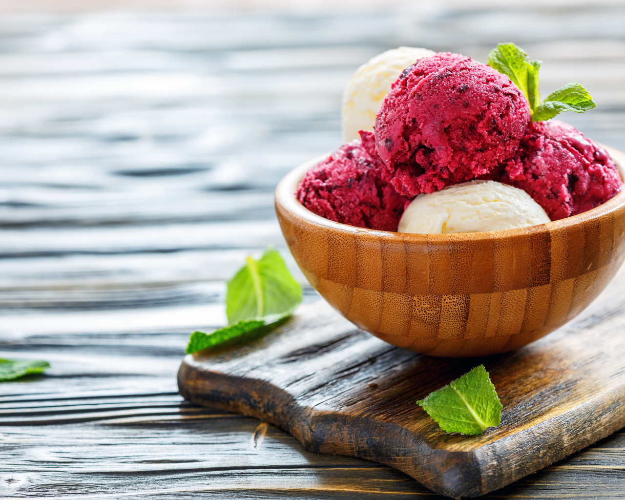 Шарики фруктового и ванильного мороженого в деревянной миске на столе