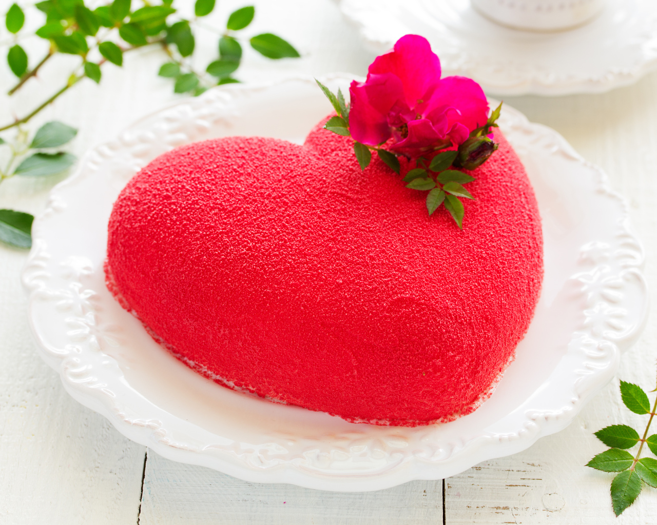 Красивый торт в форме сердца на белом блюде с красным цветком