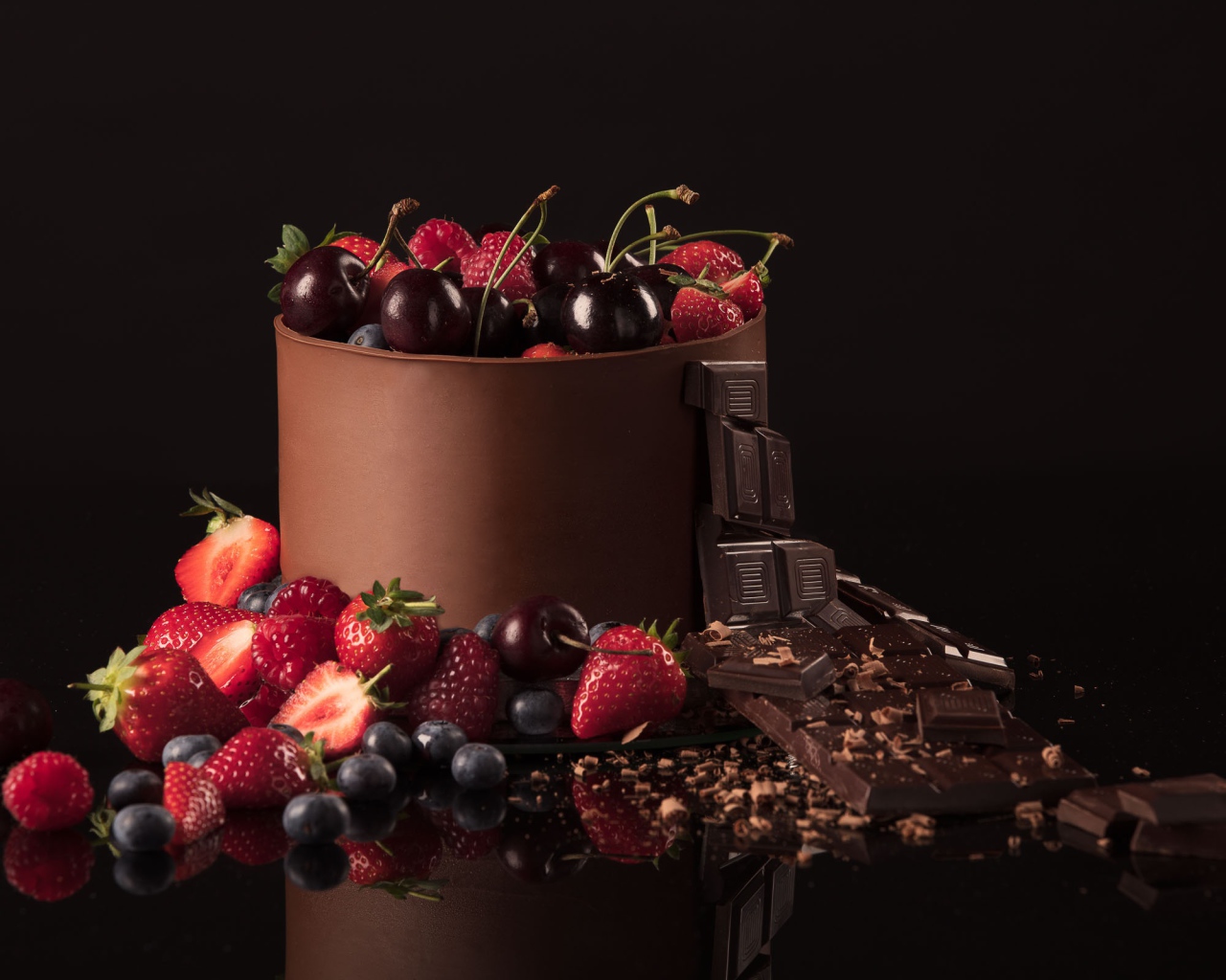 Черный шоколад с ягодами черники, малины, клубники и вишни на черном фоне