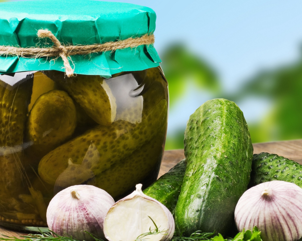 Консервированные огурцы в банке на столе со свежими огурцами и чесноком