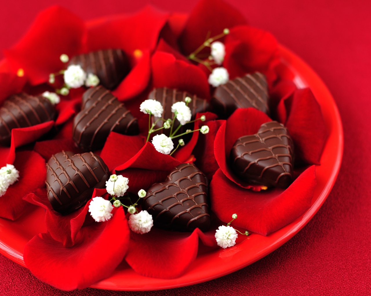 Шоколадные конфеты в форме сердца на тарелке с лепестками розы