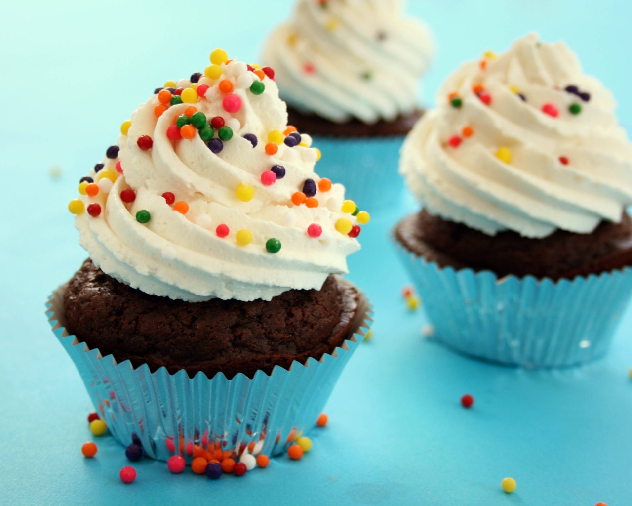 Шоколадные кексы со сливками и цветными брызгами на голубом фоне