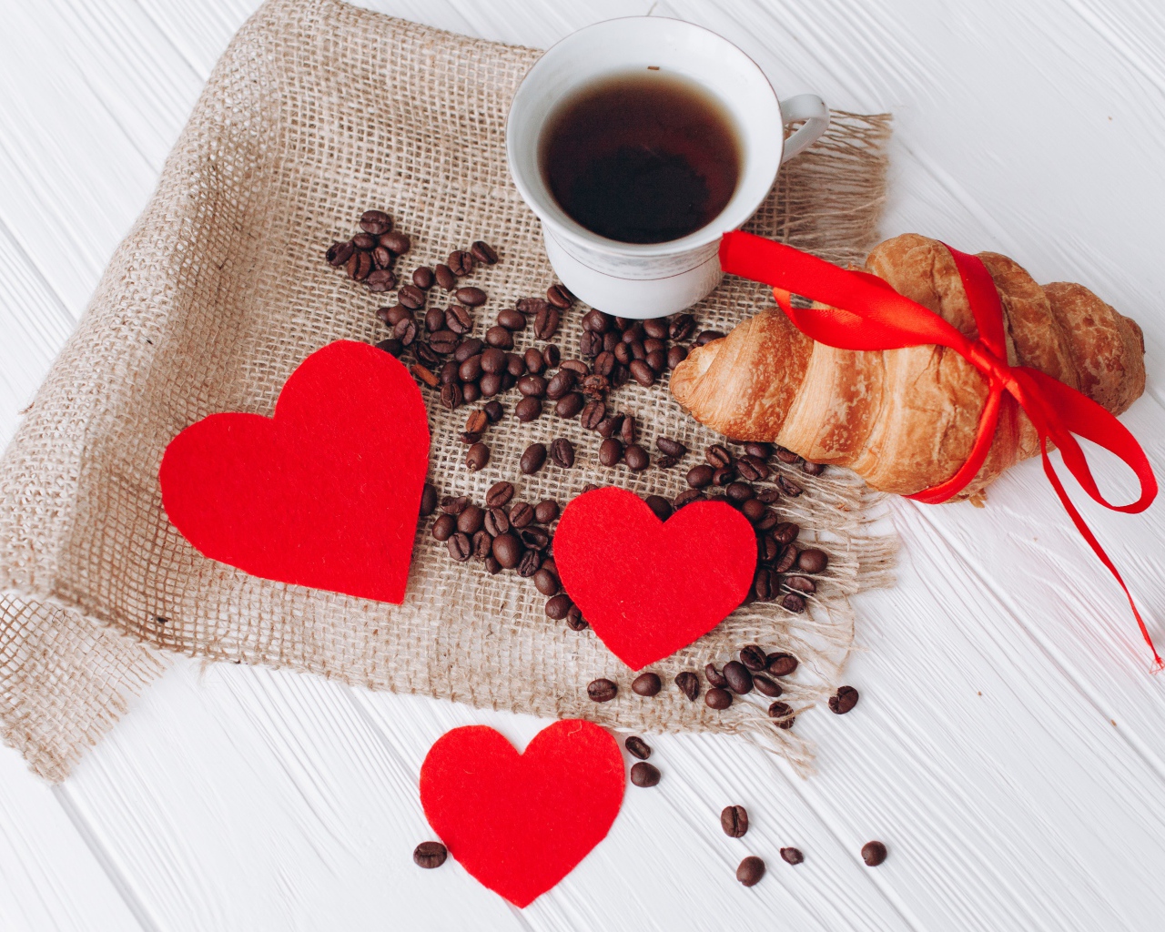 Круассан с чашкой кофе и кофейными зернами на столе с красными сердечками