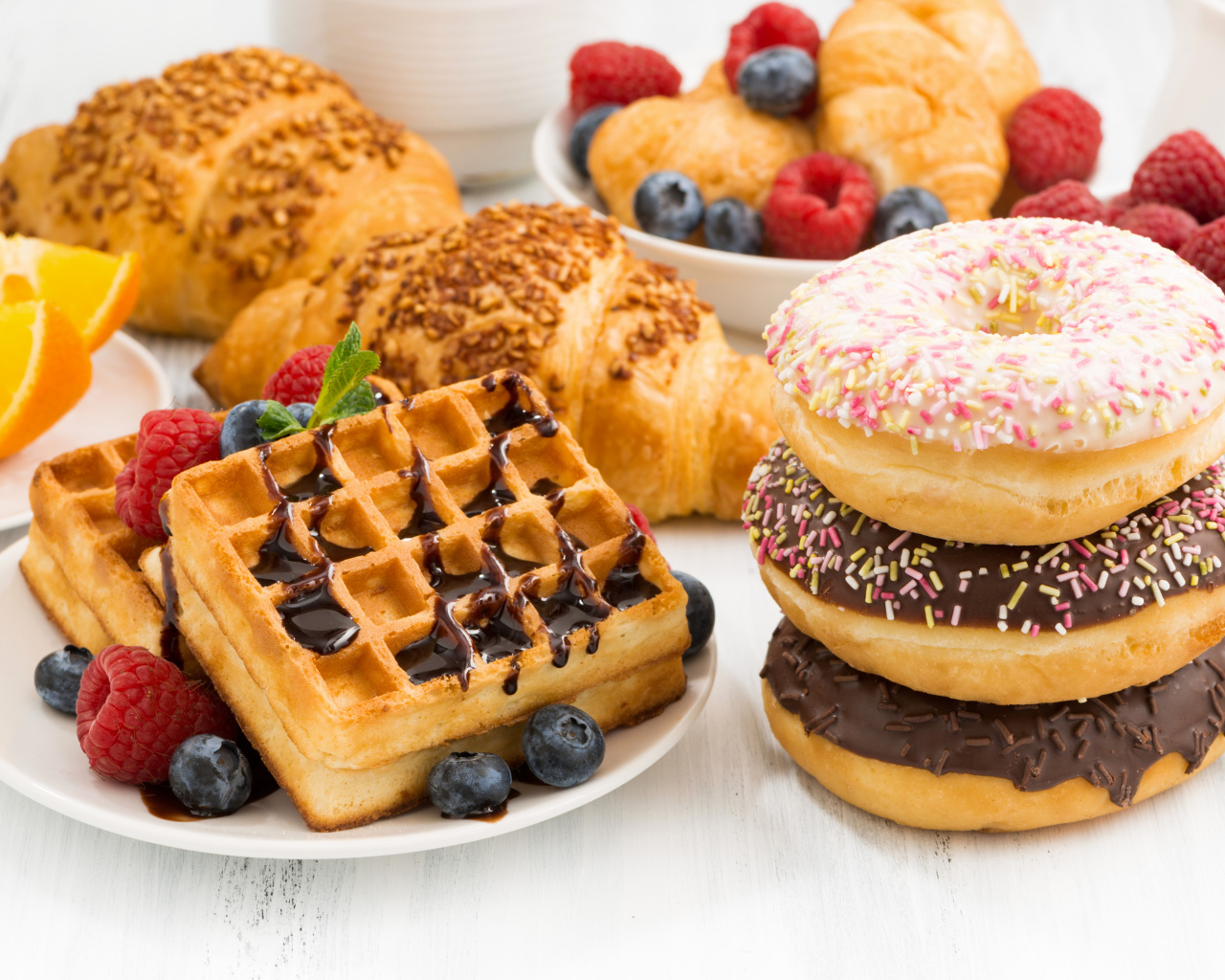 Круассаны, вафли и пончики на столе с ягодами