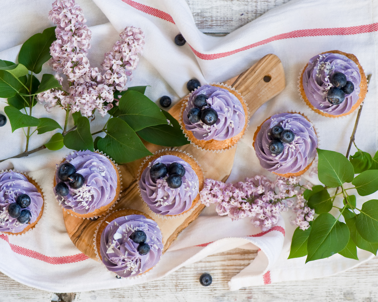 Кексы с кремом и ягодами черники на столе с ветками сирени 