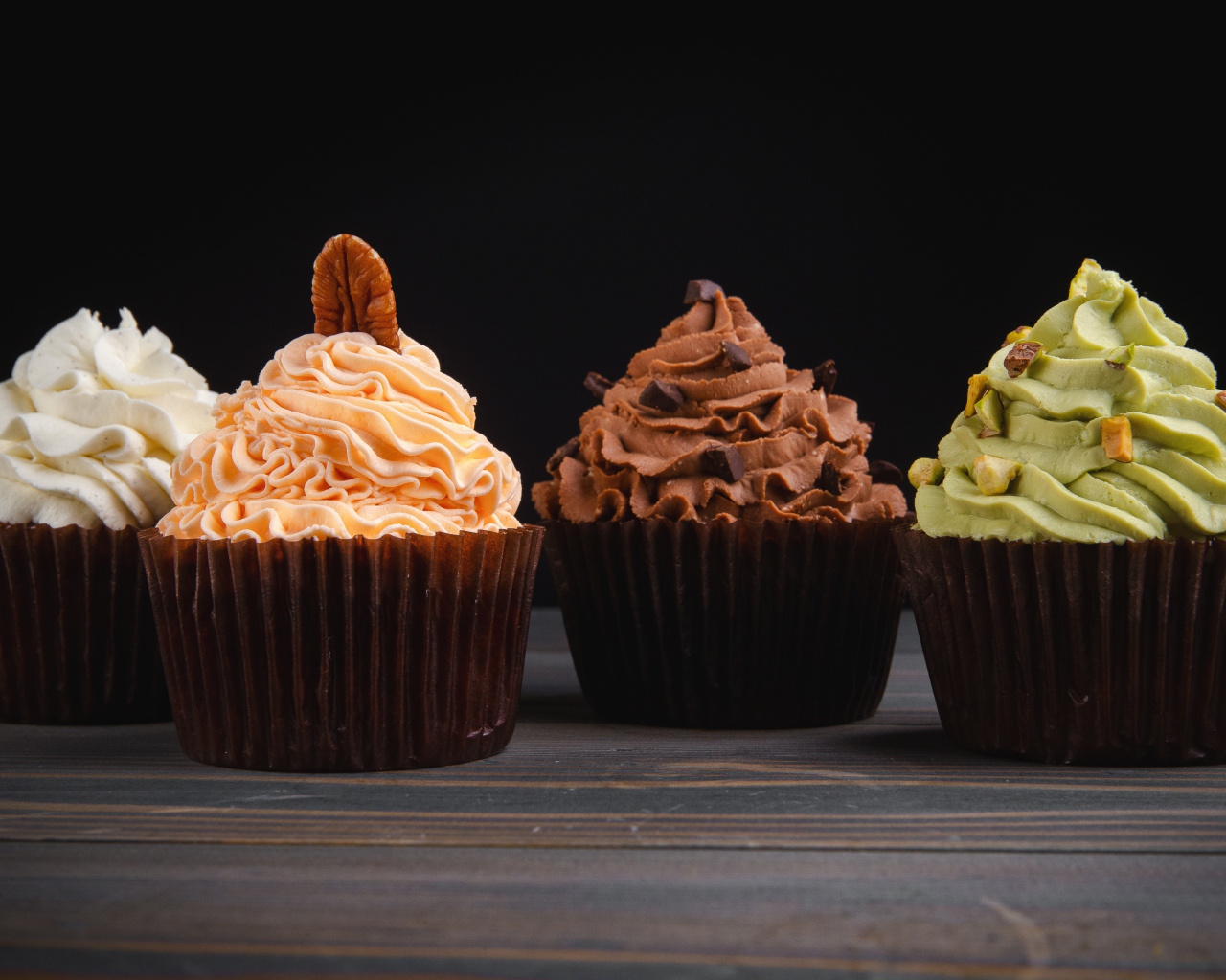 Четыре аппетитных капкейка с кремом на черном фоне