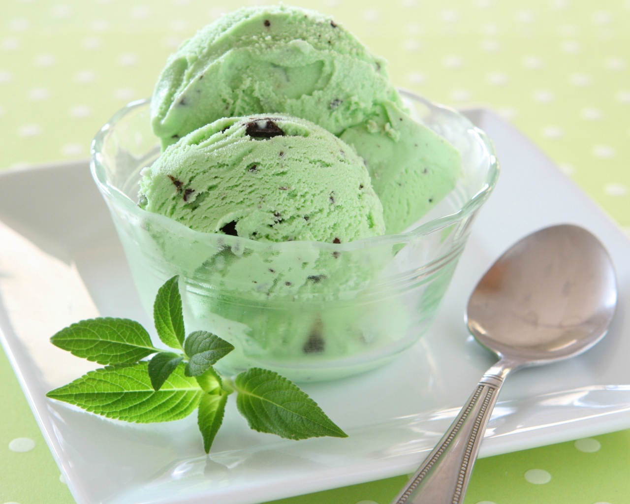 Зеленые шарики мороженого с шоколадом и мятой на тарелке с ложкой