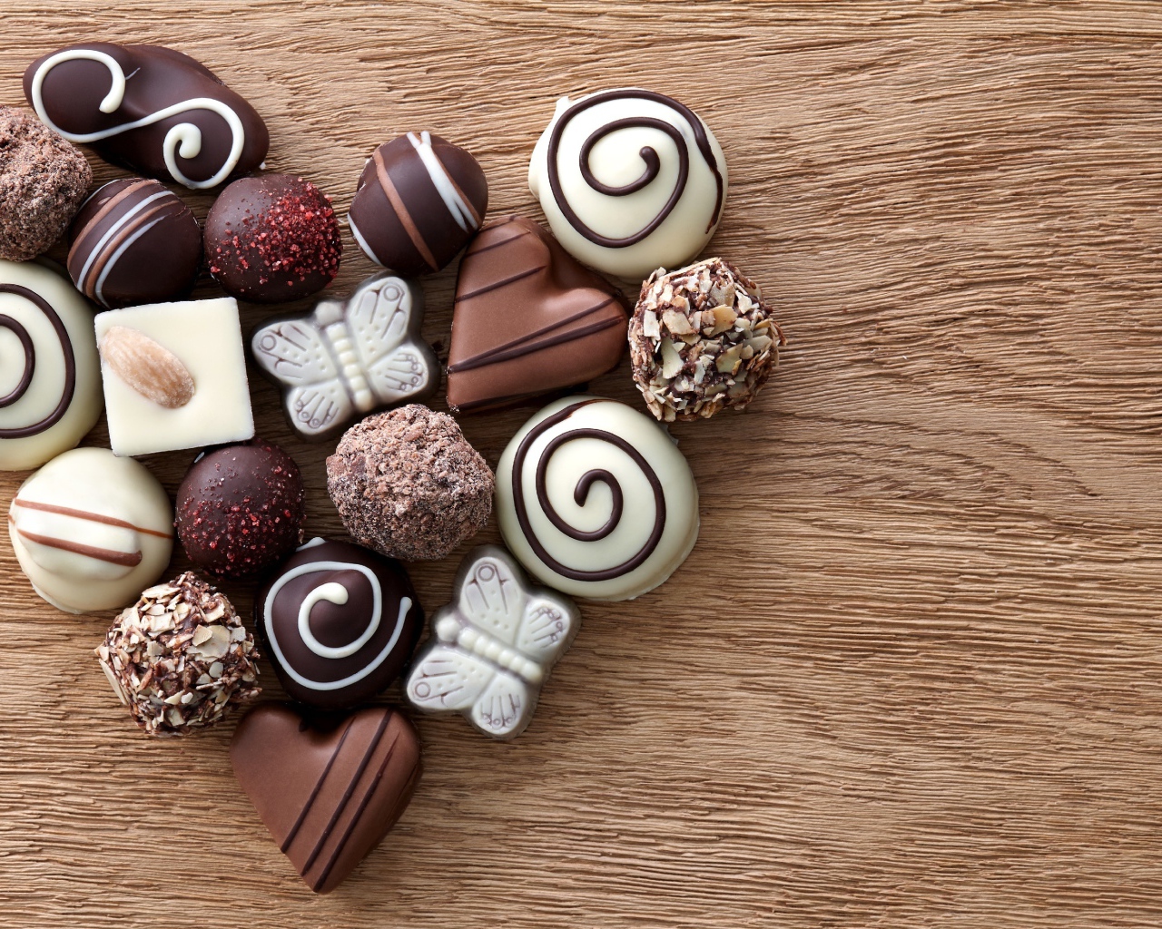 Сердце из шоколадных конфет ассорти на деревянном столе