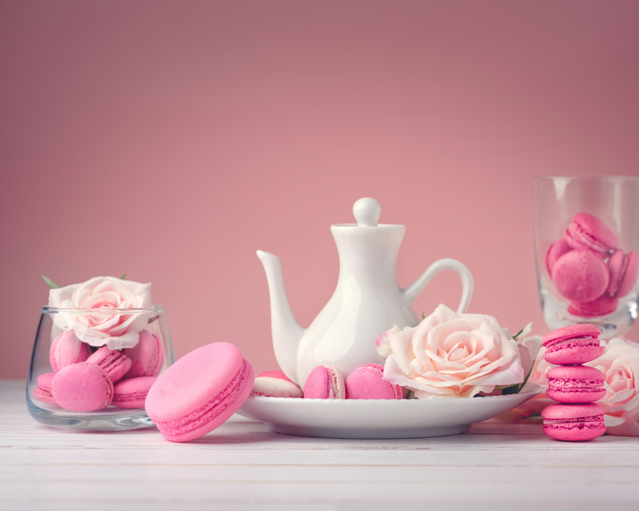 Розовый десерт макарун на столе с белый чайником и цветами розы