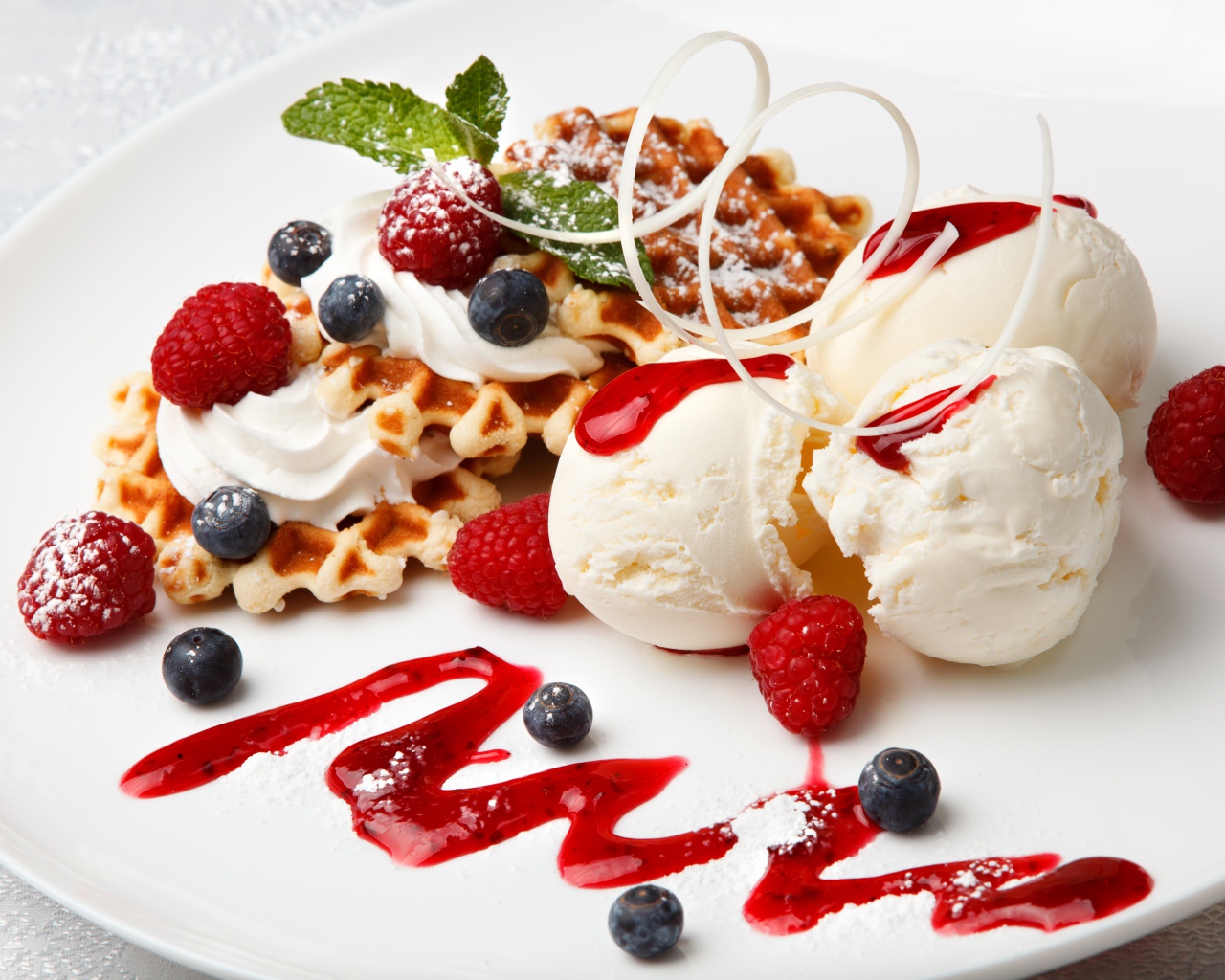 Сладкие вафли с ягодами черники и малины на белой тарелки с шариками мороженого