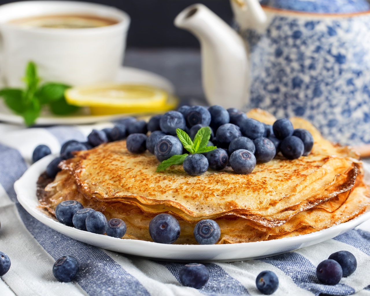 Тонкие блины с ягодами черники на столе с чаем