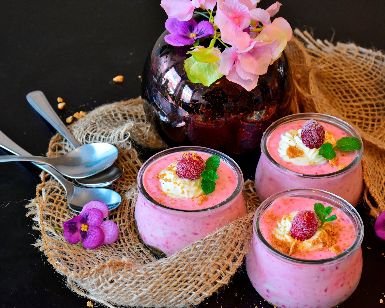 Три банки десерта с малиной на столе с цветами