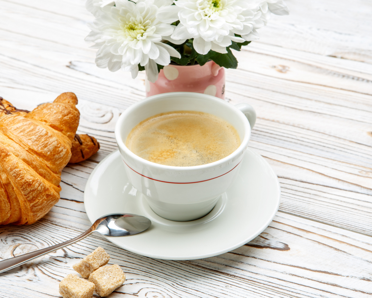 Чашка кофе и круассаны на столе с белыми хризантемами 