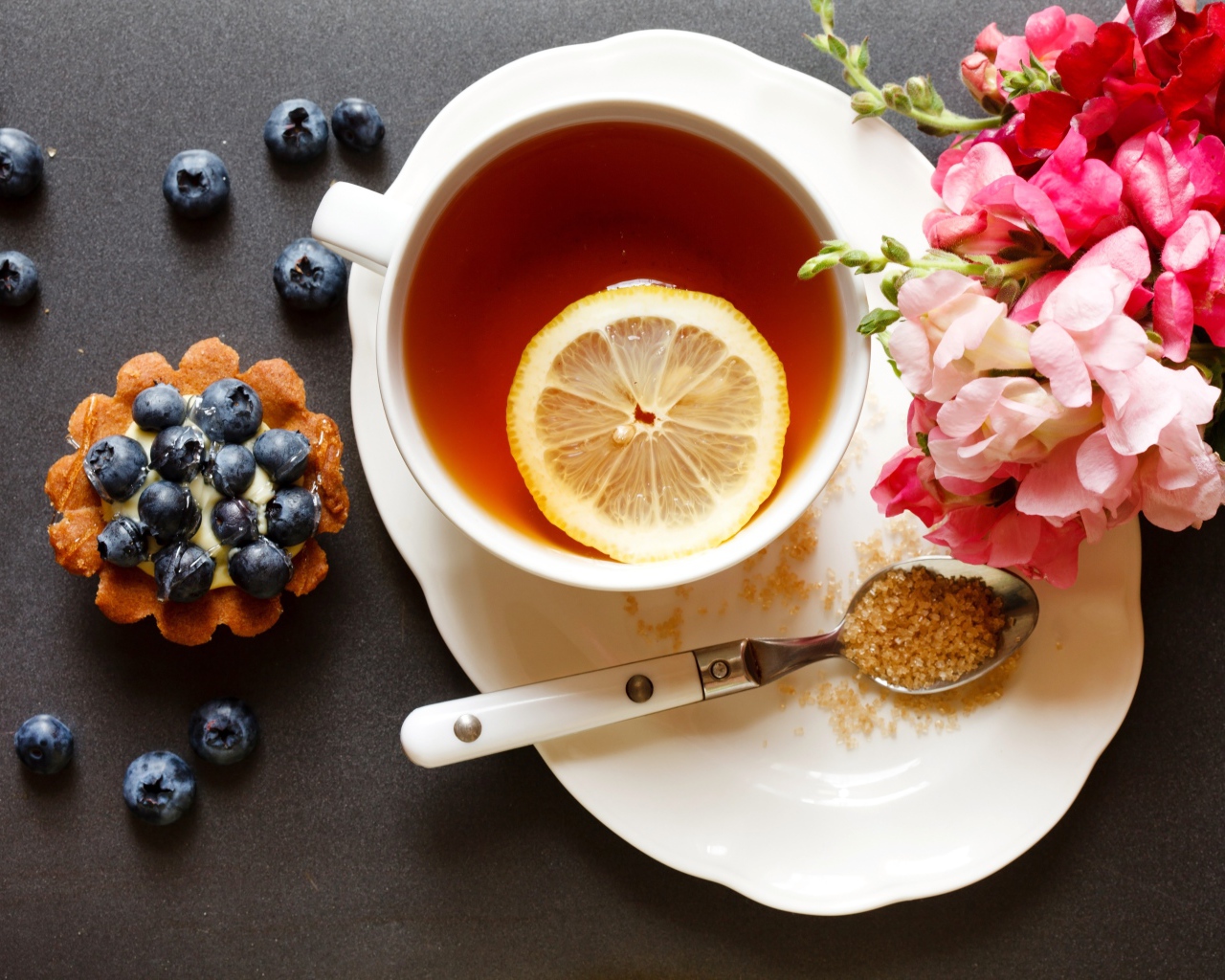 Чашка чая с лимоном на столе с кексом и цветами