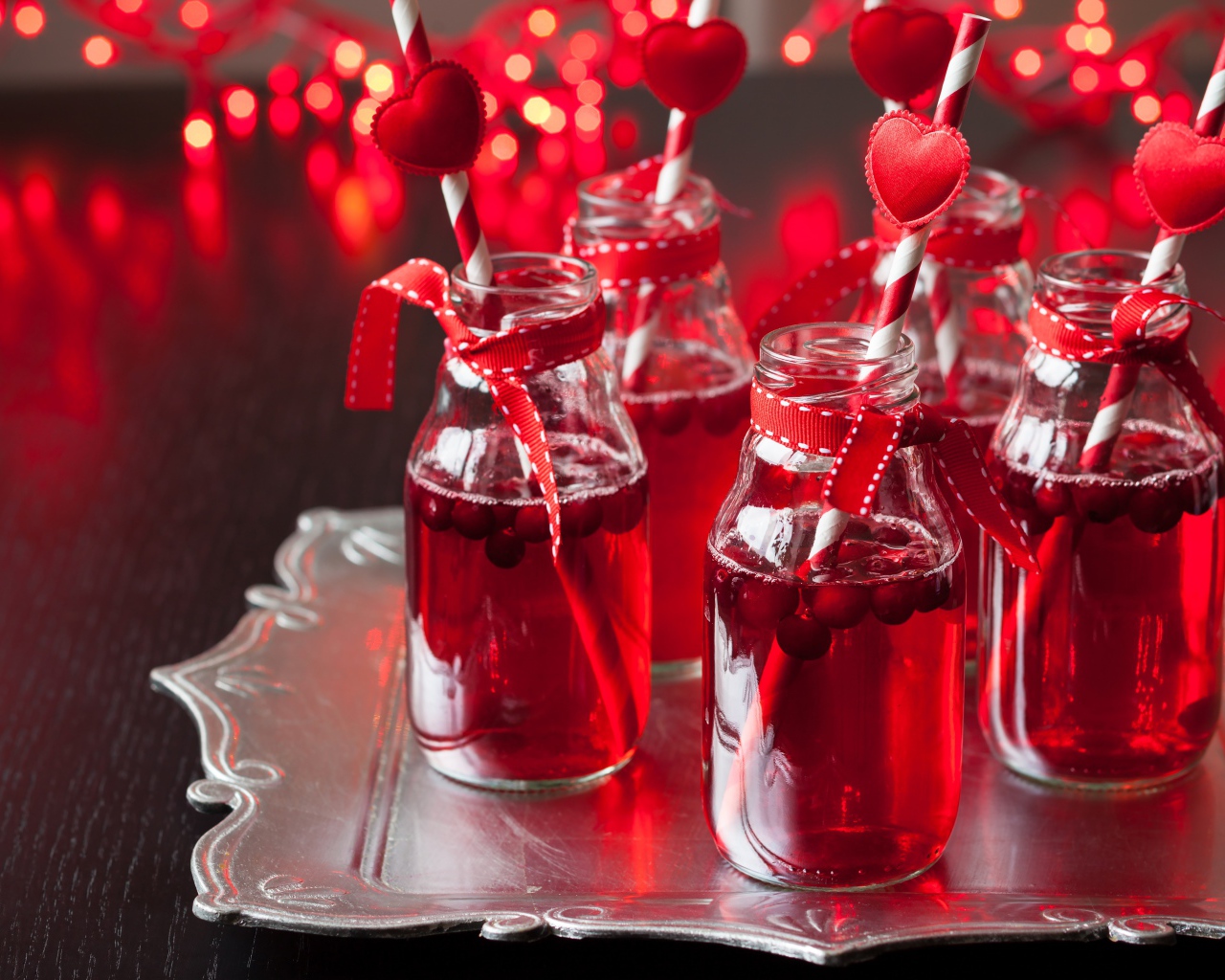 Вкусный напиток с клюквой в стеклянных бутылках на столе с трубочками