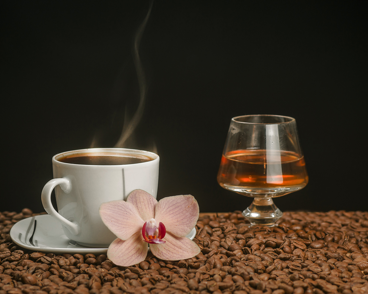 Ароматная чашка кофе на столе с бокалом виски, кофейными зернами и цветком орхидеи
