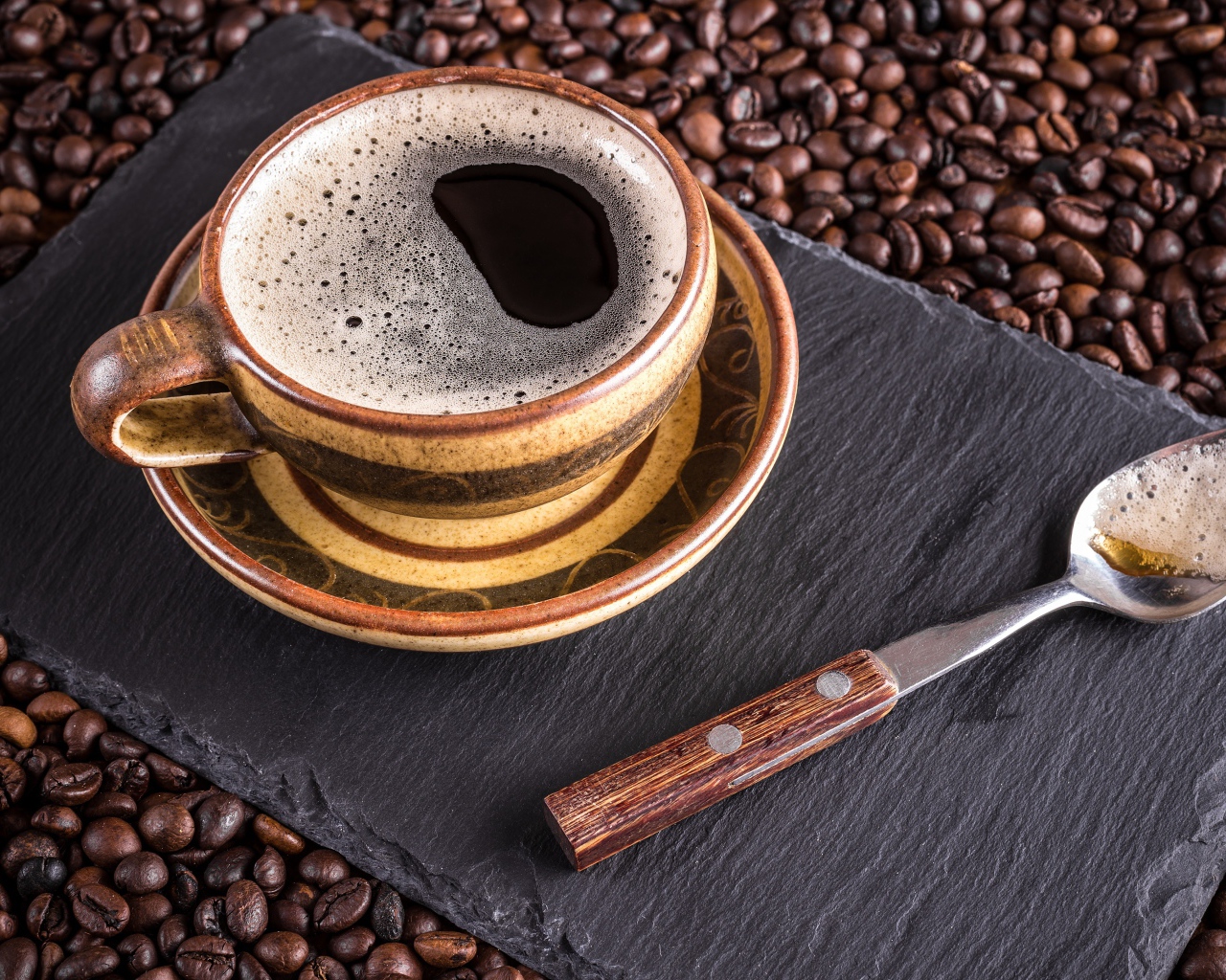 Большая чашка кофе с чайной ложкой стоят на кофейных зернах