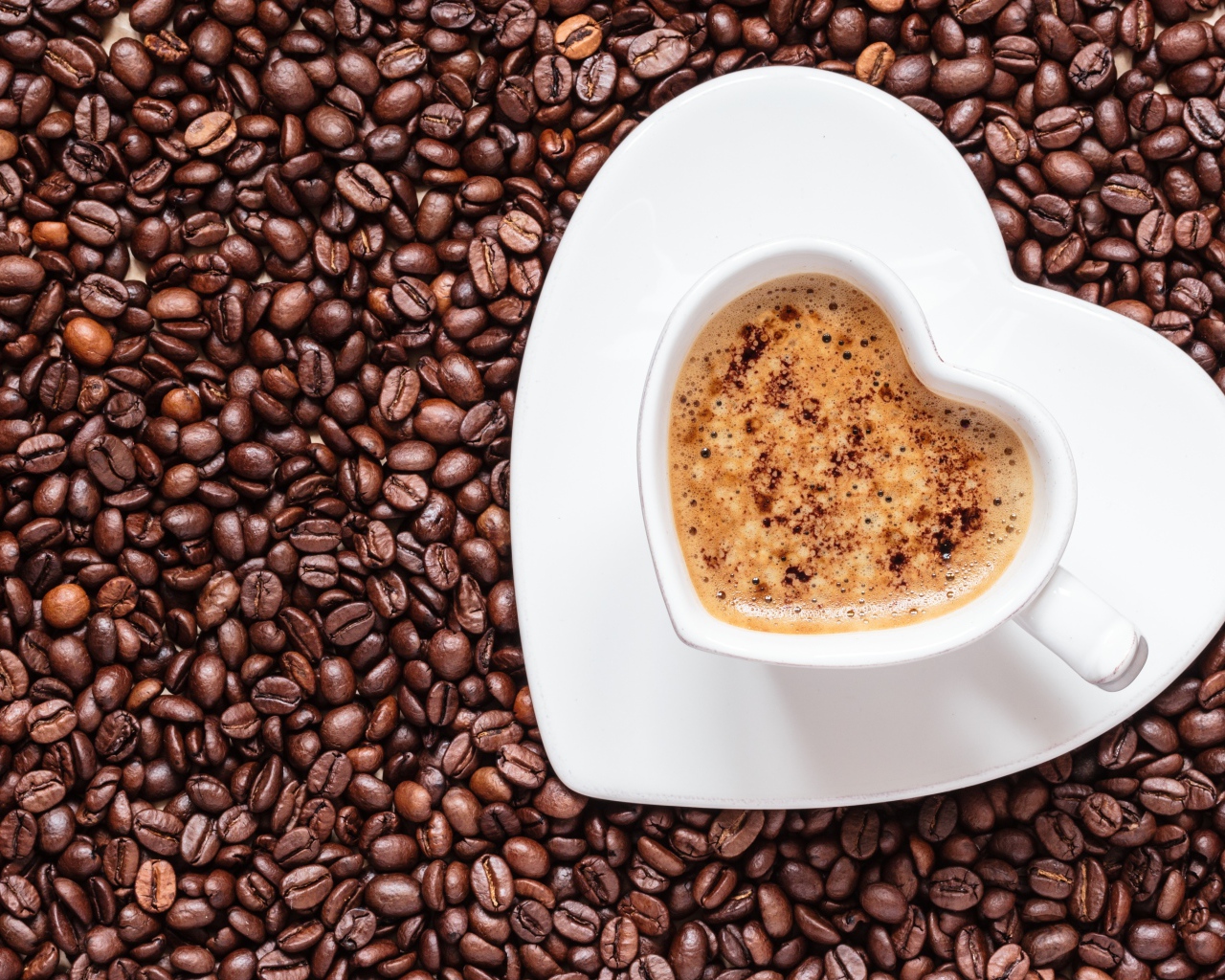 Белая чашка кофе в форме сердца стоит на кофейных зернах