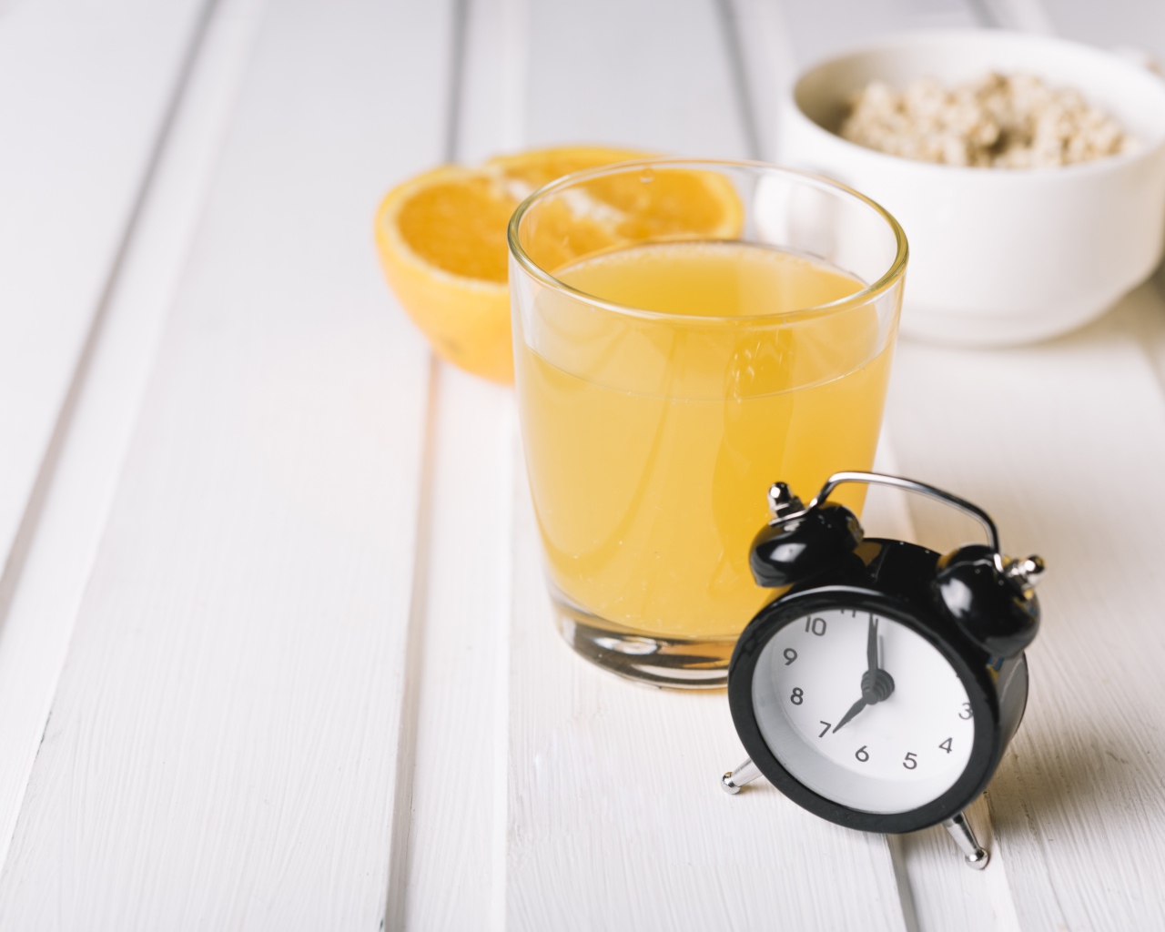 Черный будильник на столе со стаканом сока и хлопьями 