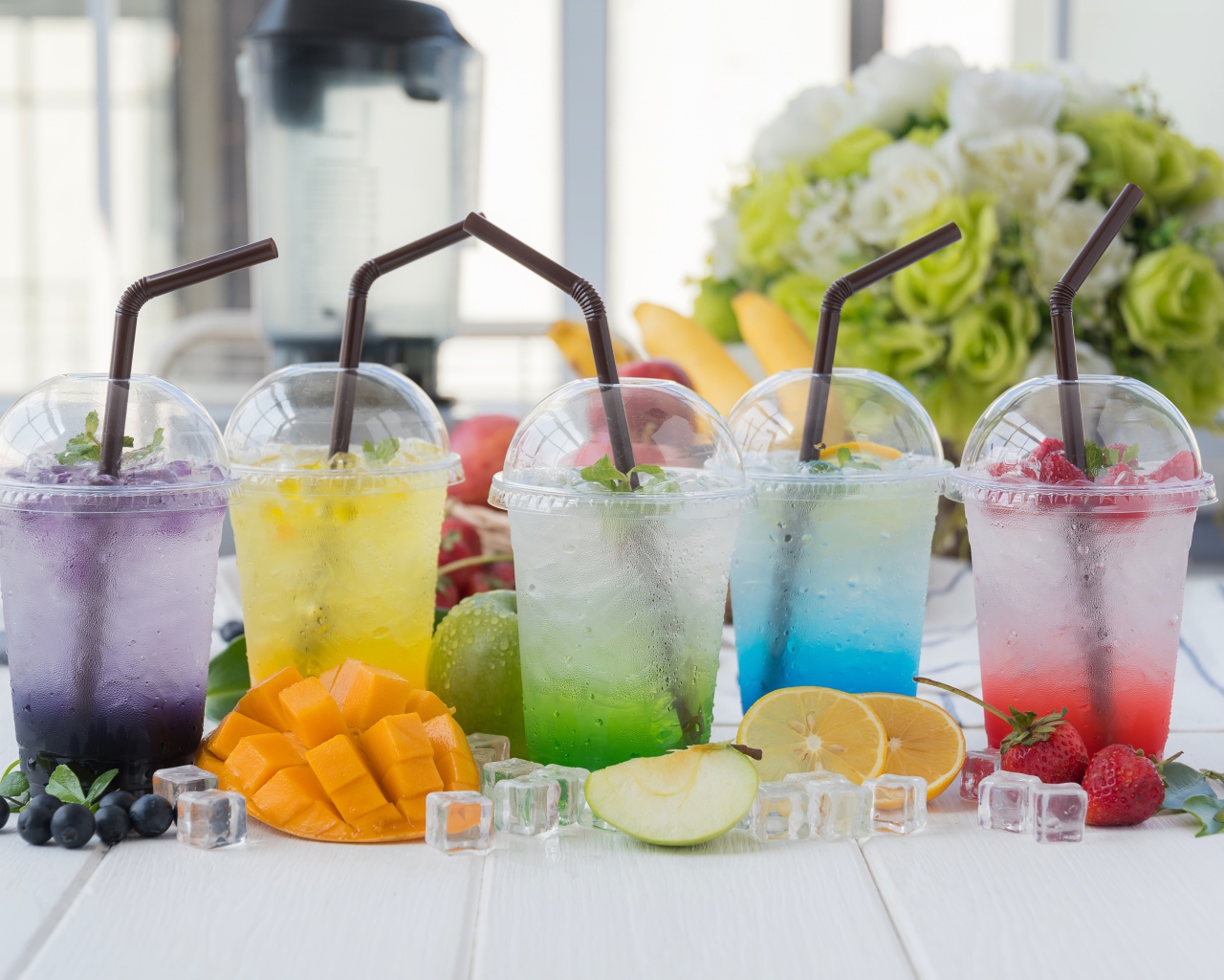 Коктейли в стаканах с трубочками на столе с кубиками льда и фруктами