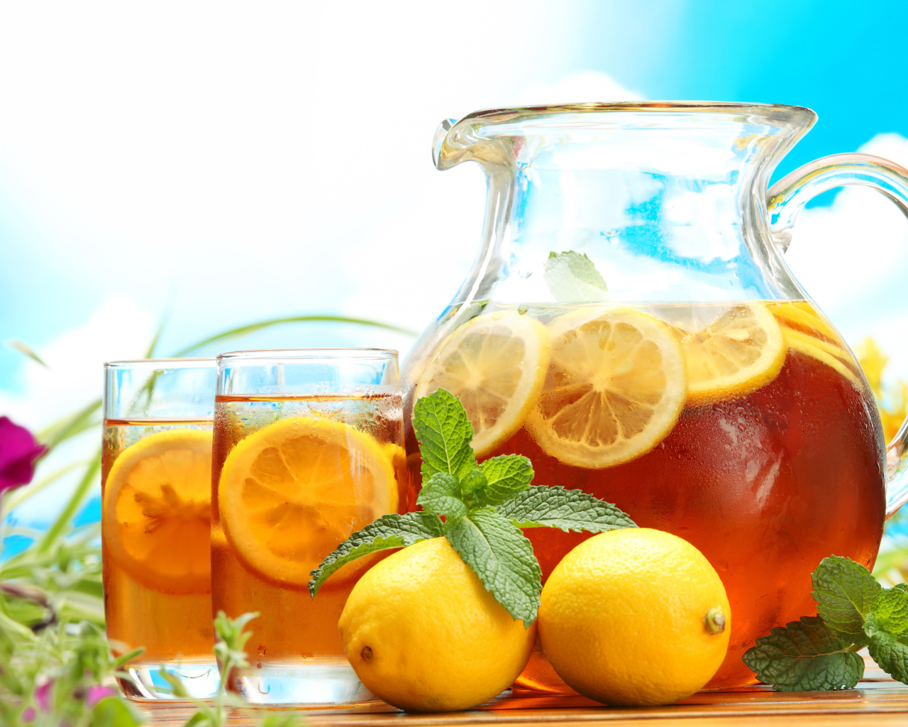 Холодный лимонад в графине на столе со стаканами и плодами лимона