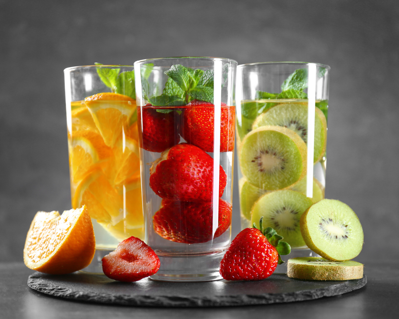 Напитки в стаканах с клубникой, киви и апельсинами на сером фоне
