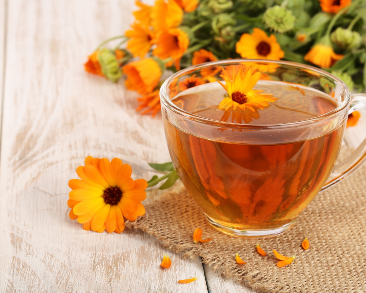 Стеклянная чашка чая с цветками календулы на столе