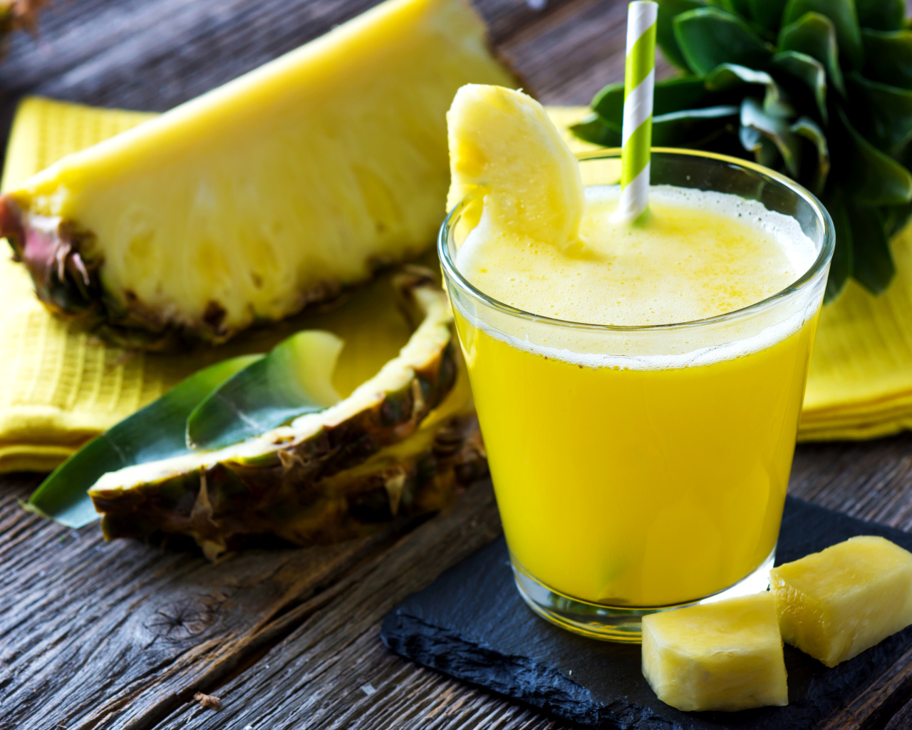 Ананасовый напиток в стакане на столе со свежими ананасами