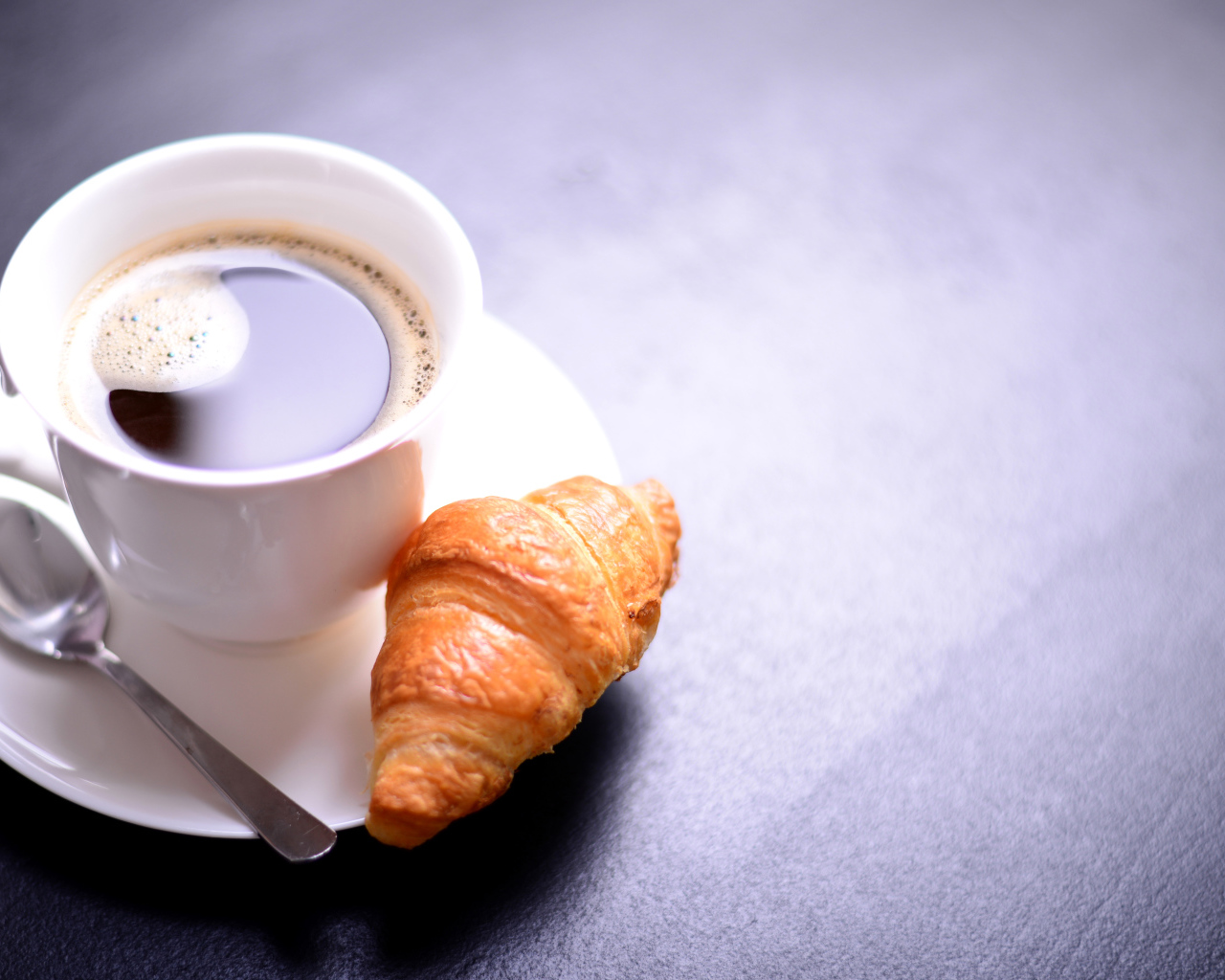 Белая чашка кофе на столе с круассаном