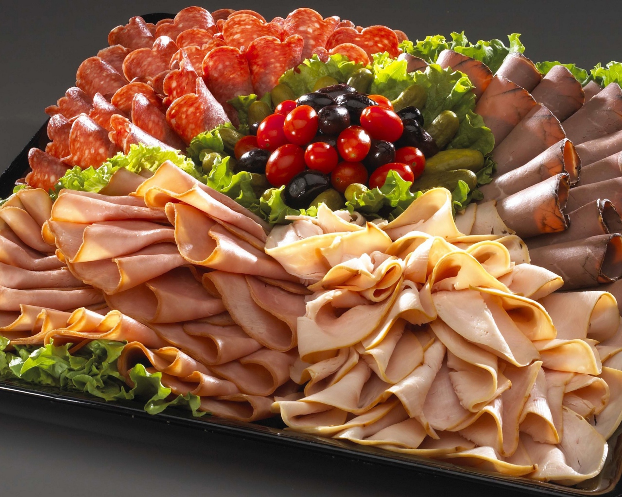 Большое блюдо с аппетитной мясной нарезкой, листьями салата и оливками