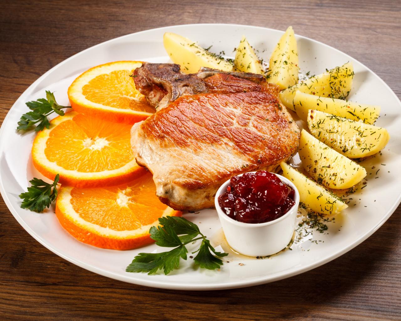 Кусок запеченного мяса с кусочками картофеля и апельсина и соусом