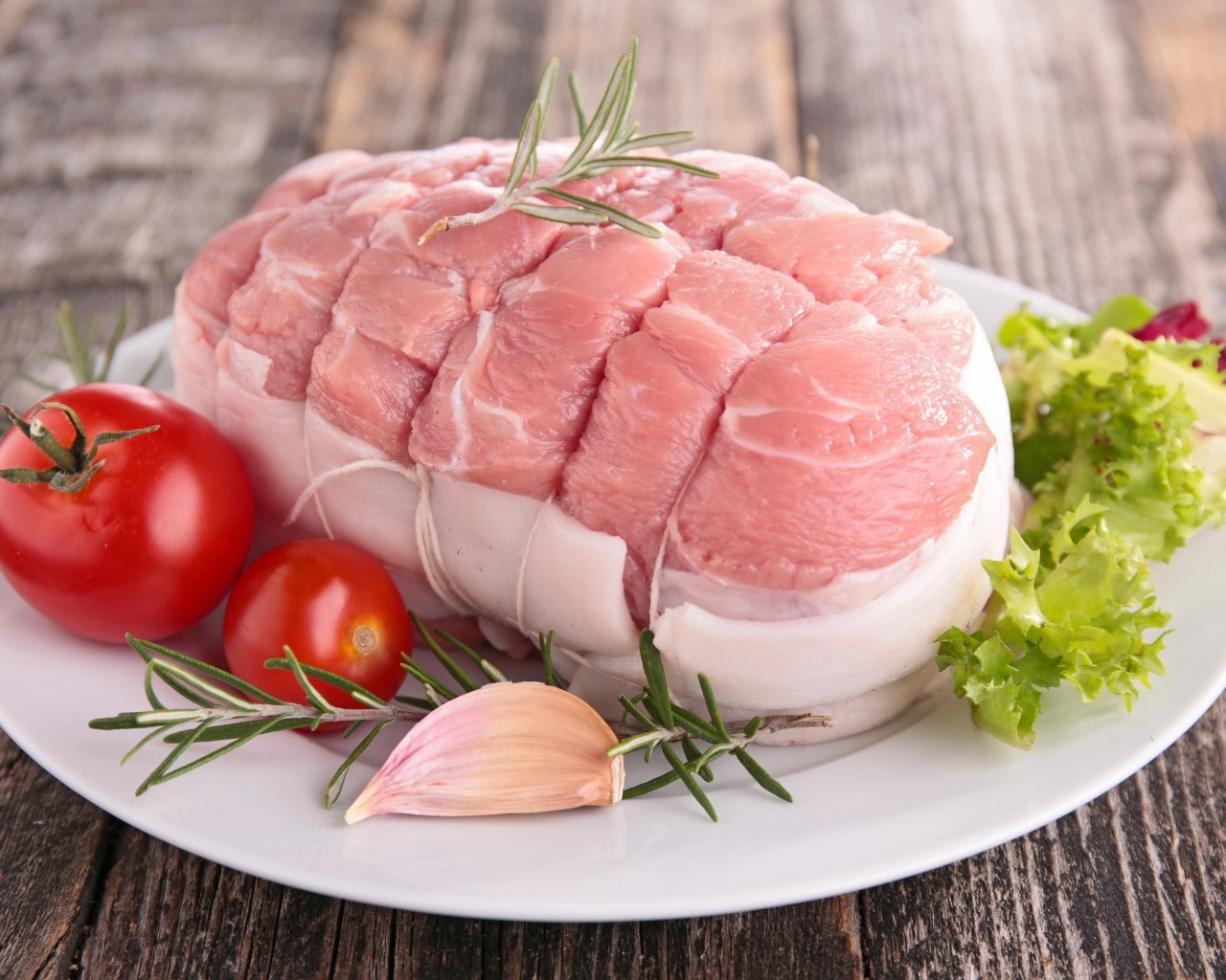 Кусок свежего мяса со свежими помидорами, чесноком и листьями салата