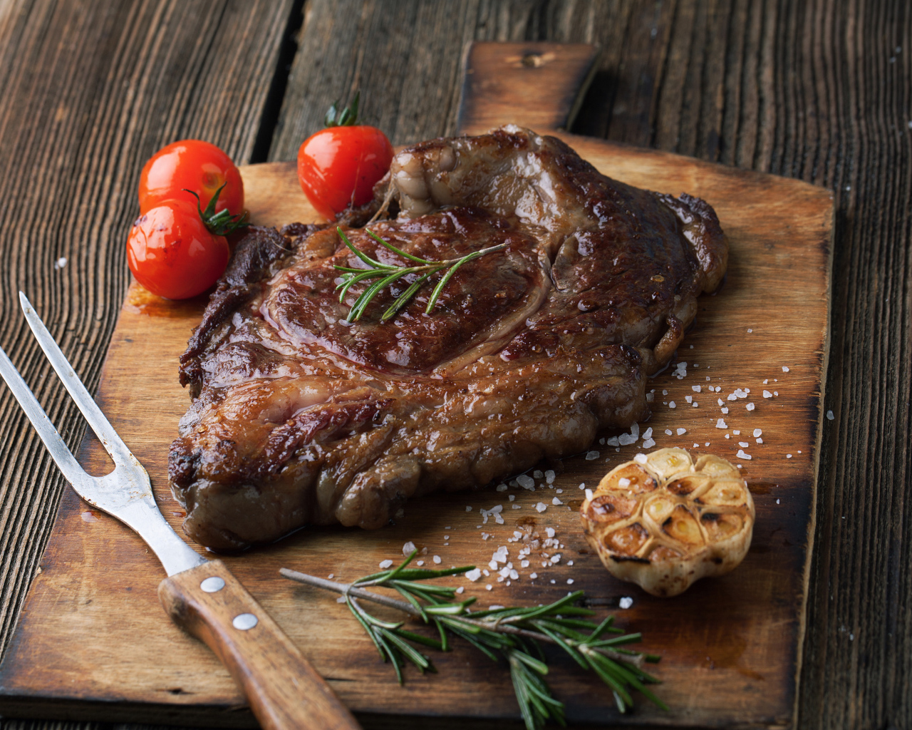 Кусок жареного мяса на разделочной доске с помидорами и чесноком