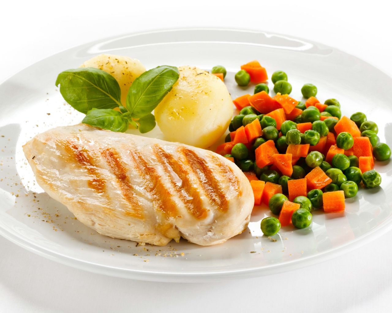 Куриная грудка на белой тарелке с картофелем, морковью и зеленым горошком