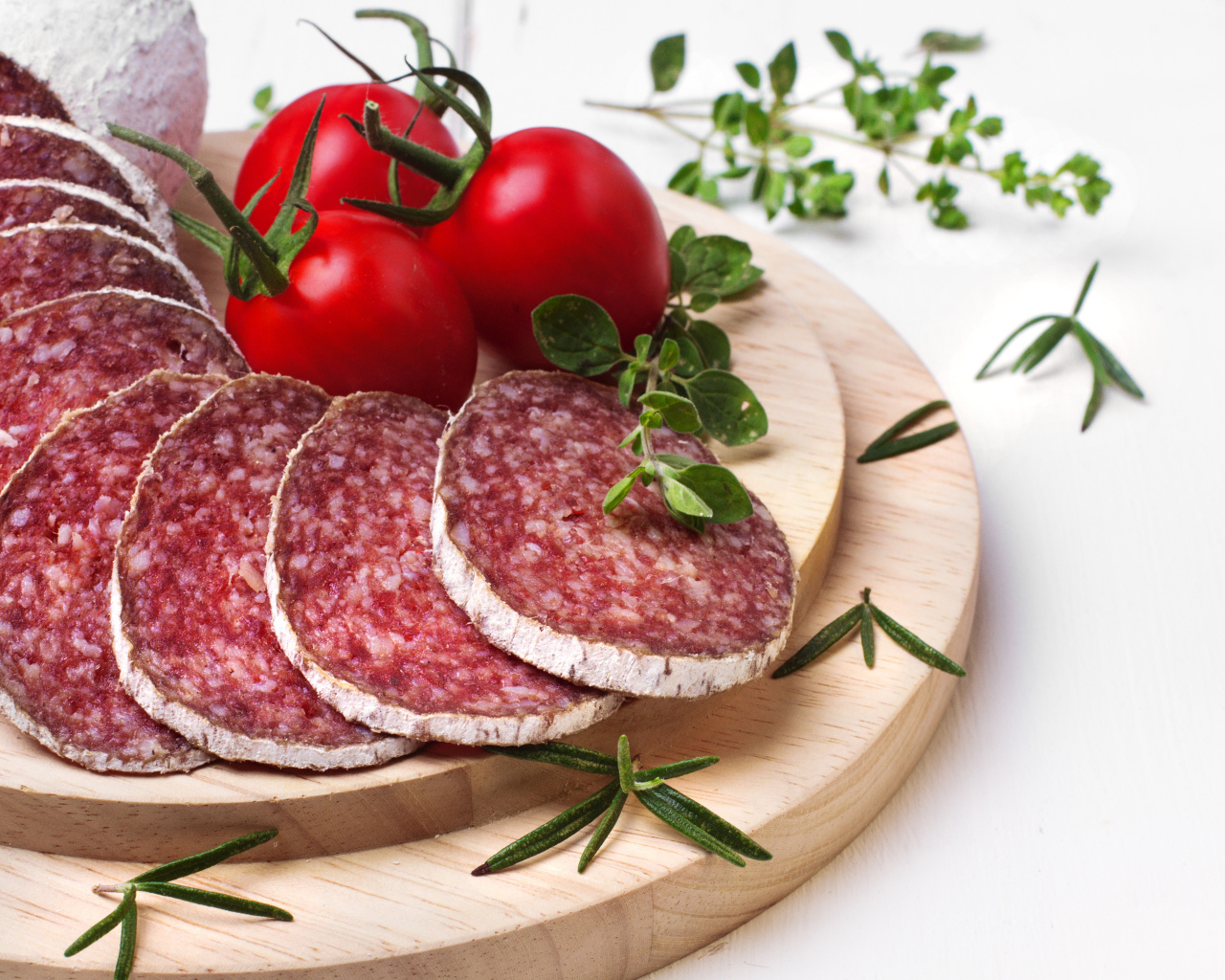 Вкусная колбаса на разделочной доске с помидорами и зеленью 