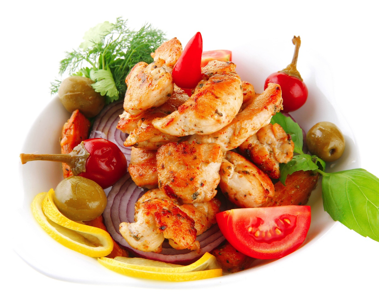 Жареные кусочки курицы на тарелке с овощами и зеленью 