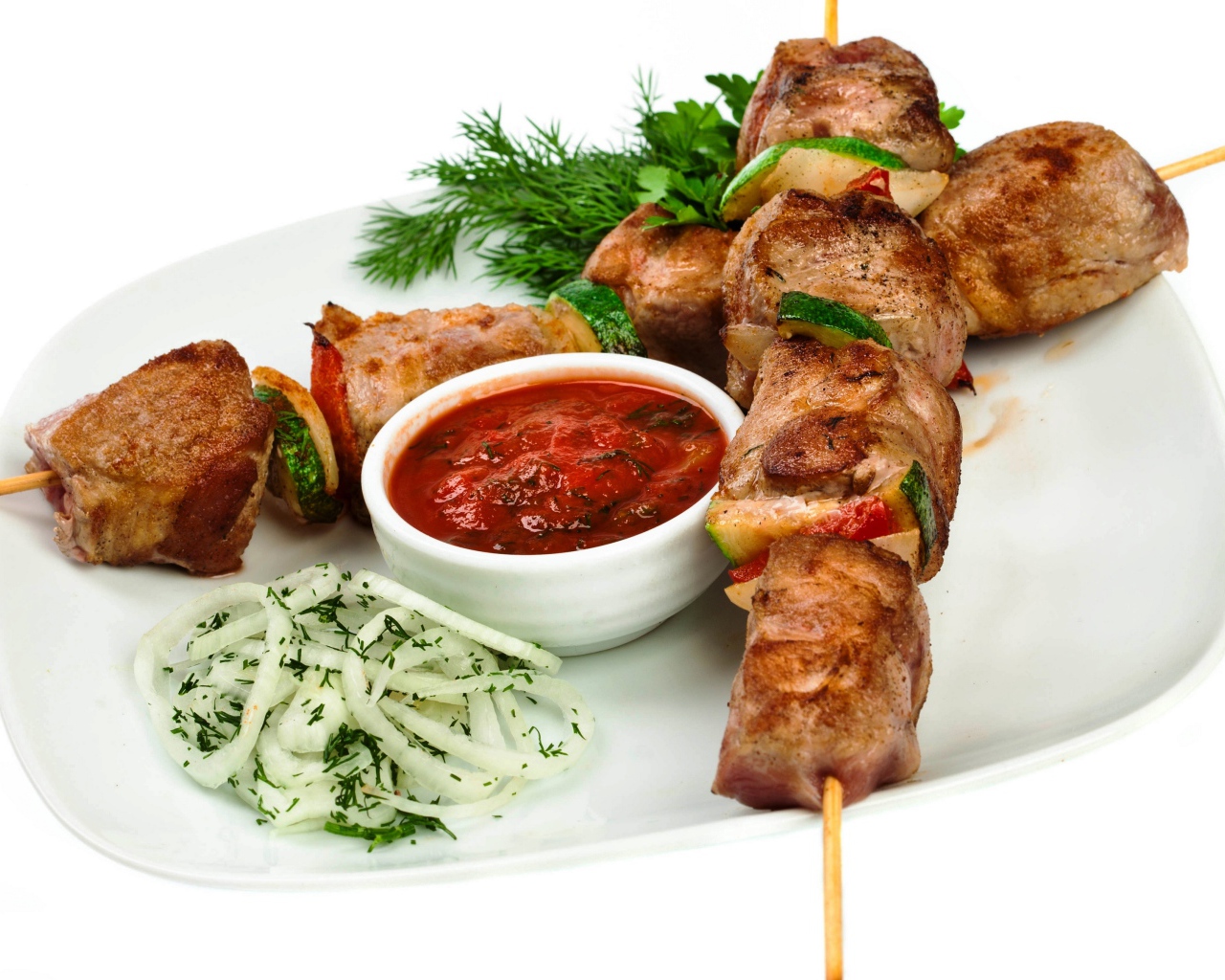 Skewers on a white plate with sauce, herbs and onions