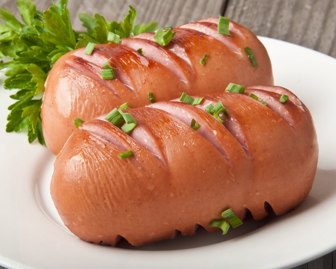 Два жареные сардельки на большой белой тарелке с зеленью 