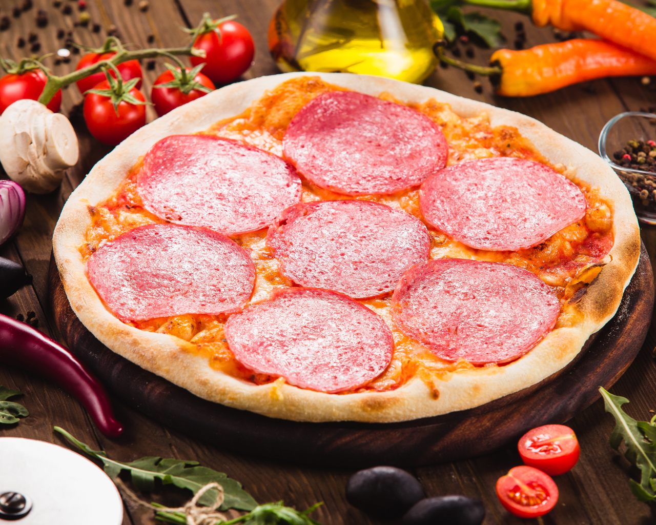 Пицца с салями на столе с овощами 