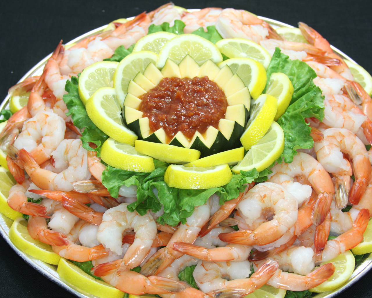 Вареные креветки с лимоном и соусом на большой тарелке