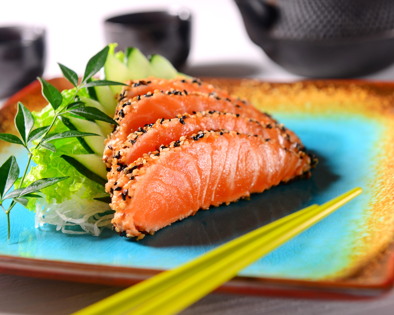 Красная рыба с листьями салата и свежими огурцами на тарелке с палочками