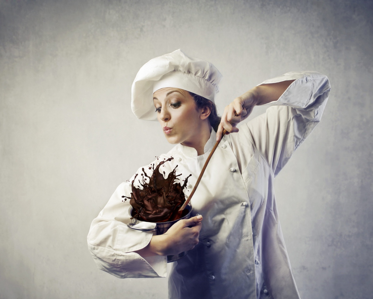 Женщина повар мешает шоколад в посуде на сером фоне
