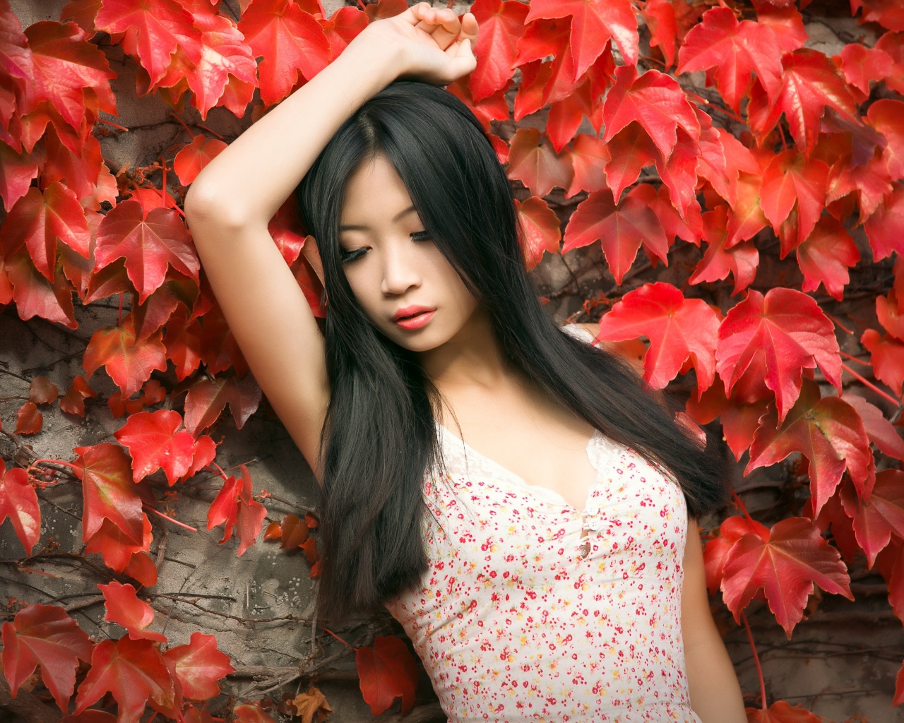 Молодая девушка азиатка стоит у стены с красными листьями