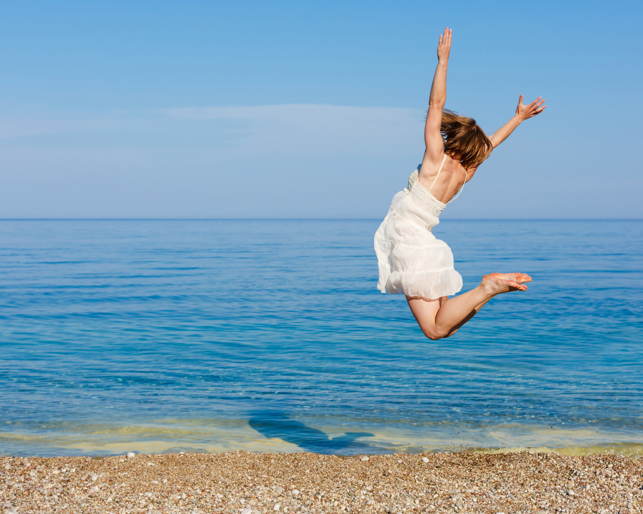 Молодая девушка в белом платье делаем прыжок на песке у моря