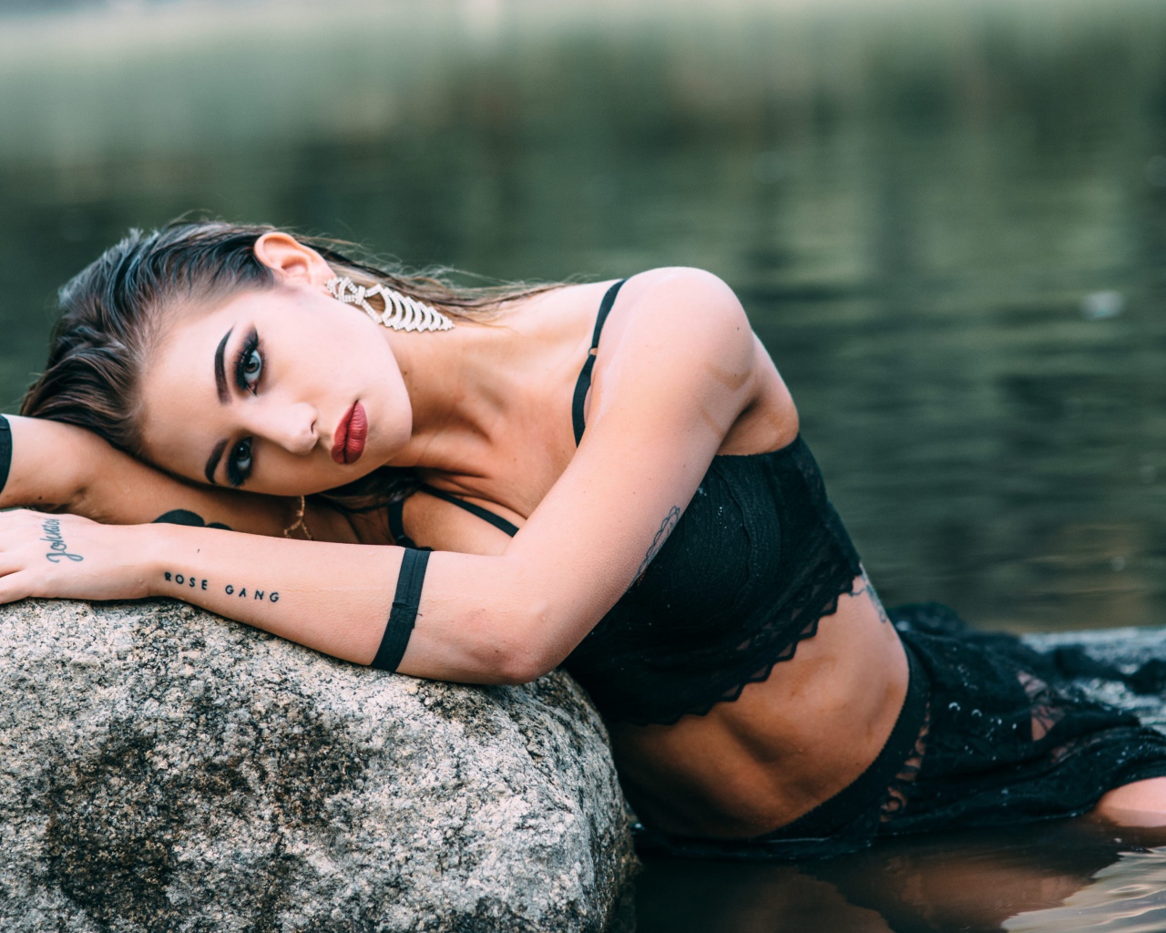 Молодая девушка с татуировками сидит у камня в воде