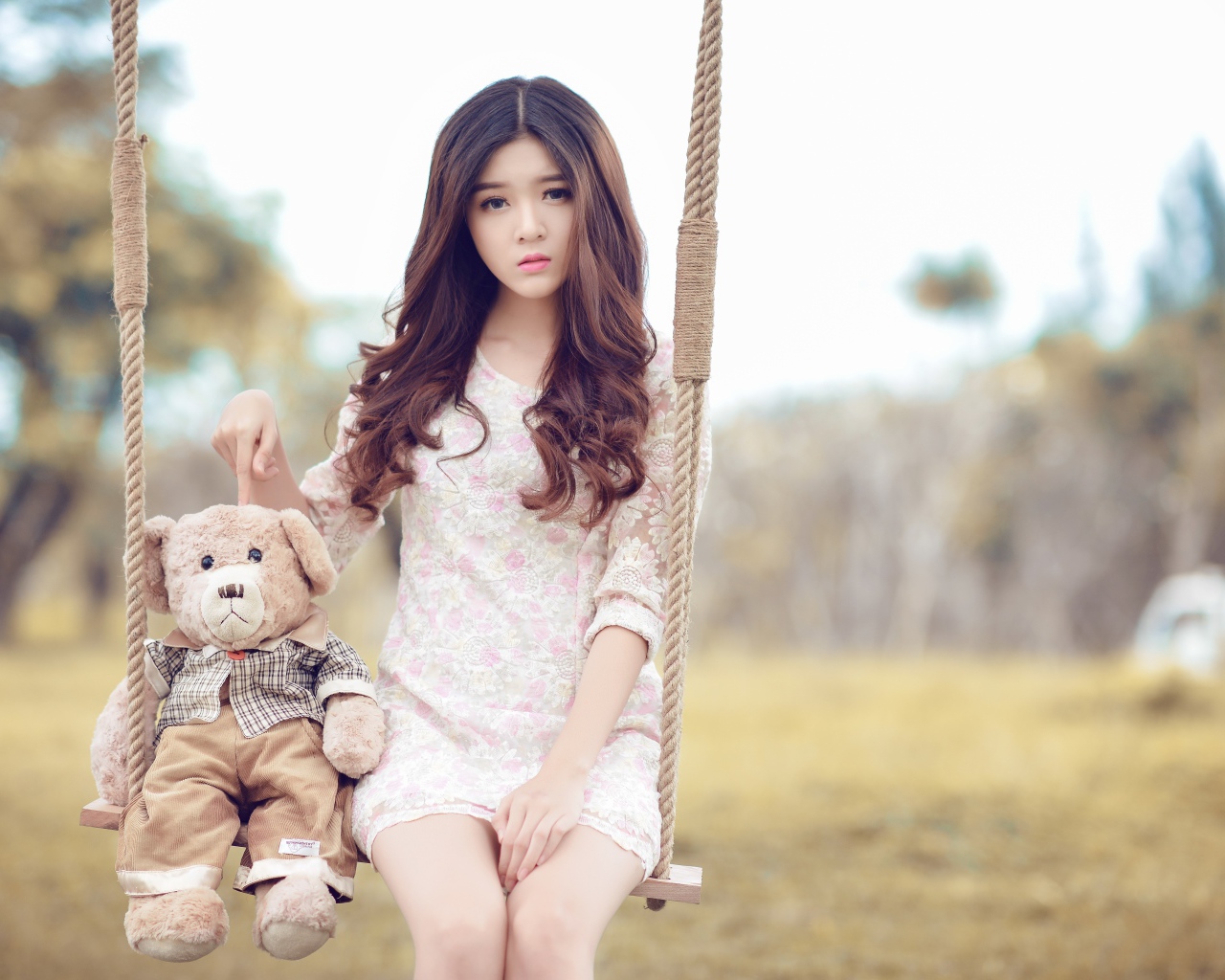 Девочка азиатка сидит на качели с плюшевым мишкой