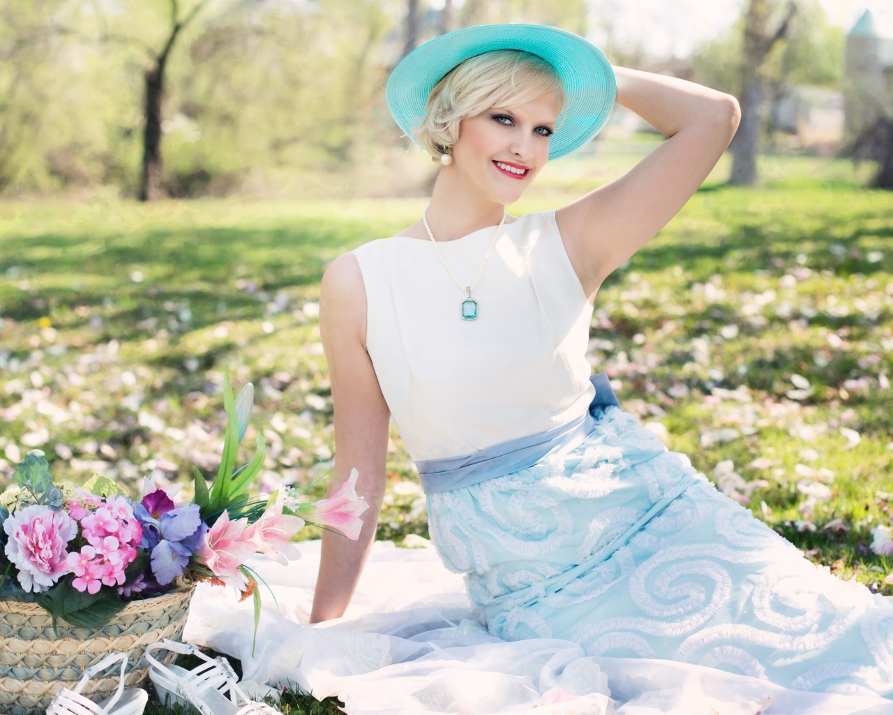 Красивая блондинка в голубой шляпке сидит в парке на траве