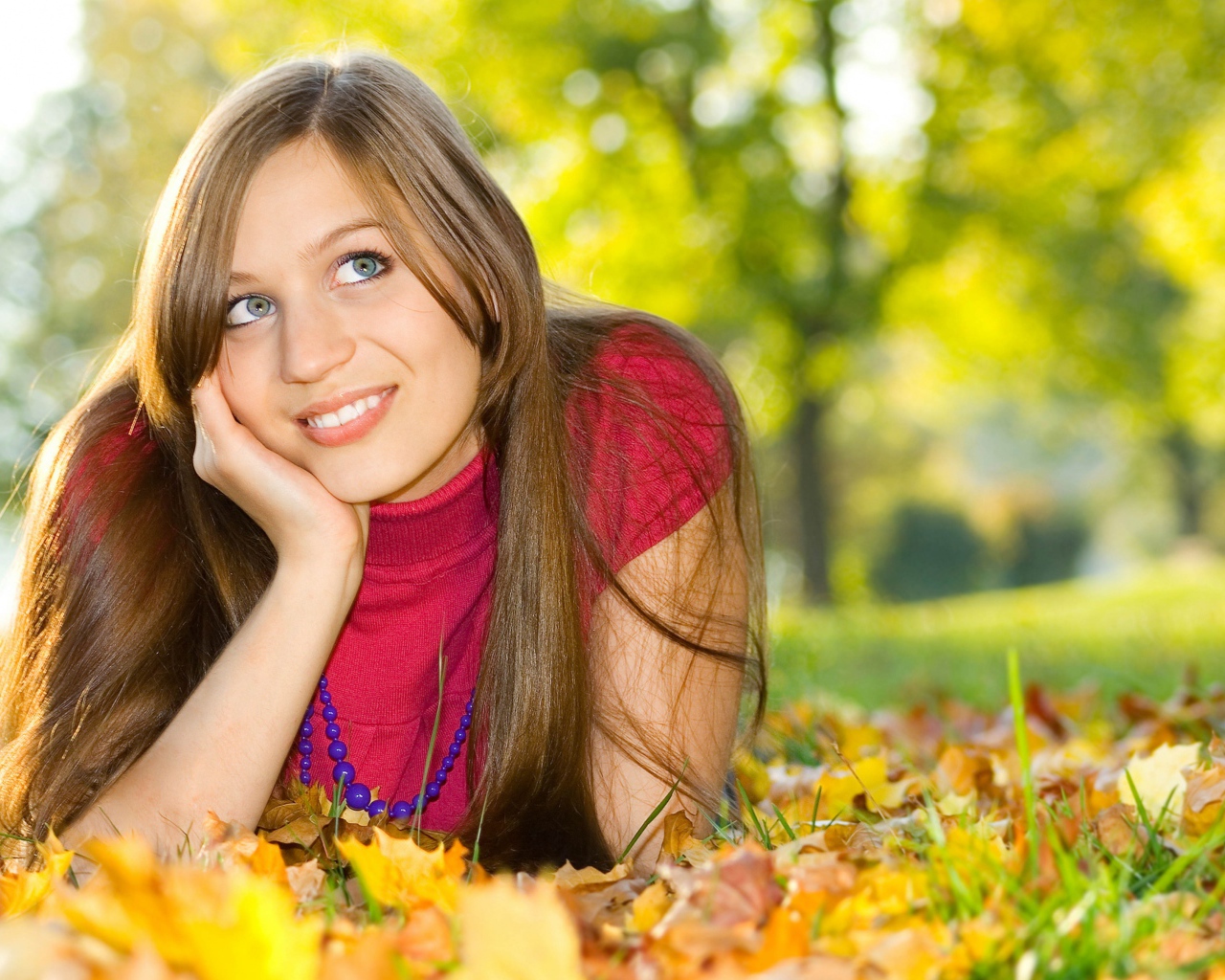 Красивая голубоглазая шатенка лежит на траве с желтыми листьями